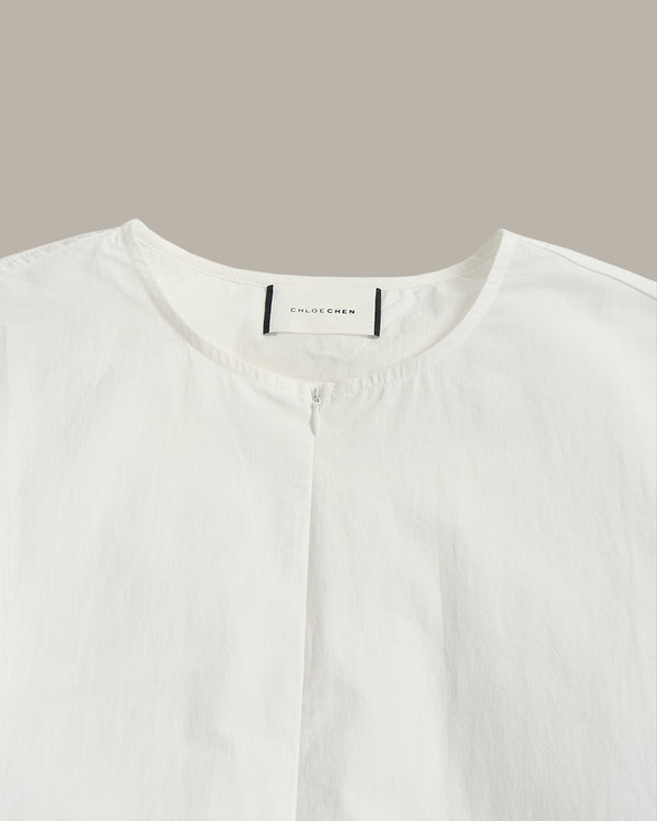 Close-up of a white button-front top with a round neckline and a visible neck label reading 'COLORFEDEN' against a plain taupe background.