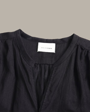 Close-up of a black women's blouse with a round neckline, gathered shoulders, and a white neck label reading 'CHILDREN'.