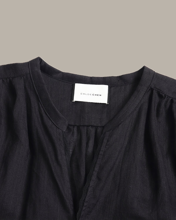 Close-up of a black women's blouse with a round neckline, gathered shoulders, and a white neck label reading 'CHILDREN'.