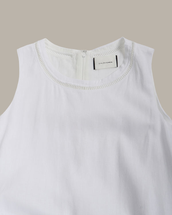 White sleeveless top with a brand label on a beige background