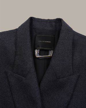 Close-up of a dark charcoal gray wool-blend blazer by Chloe Chen, showing the collar, lapels, and a black brand label with a silver-tone metal accent.