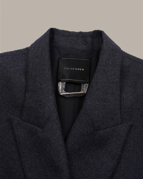 Close-up of a dark charcoal gray wool-blend blazer by Chloe Chen, showing the collar, lapels, and a black brand label with a silver-tone metal accent.
