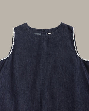 Close-up of a sleeveless dark navy blue top or dress with white braided trim along the armholes, shown against a plain warm gray background.