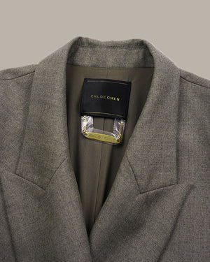 Close-up of a gray textured wool blazer collar with a black CHLOE CHEN brand label visible inside the neck, set against a solid taupe background.