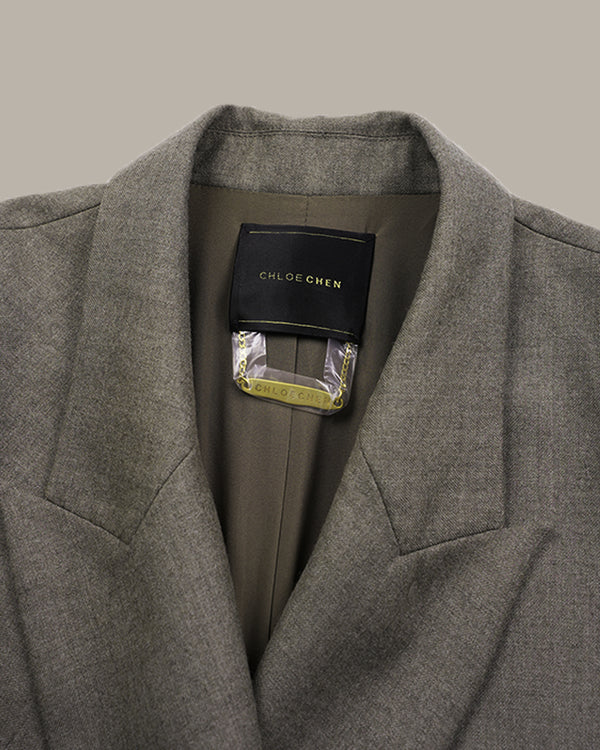 Close-up of a gray textured wool blazer collar with a black CHLOE CHEN brand label visible inside the neck, set against a solid taupe background.