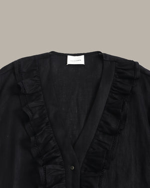 close up of a black ruffle blouse with ruffled details on a beige background