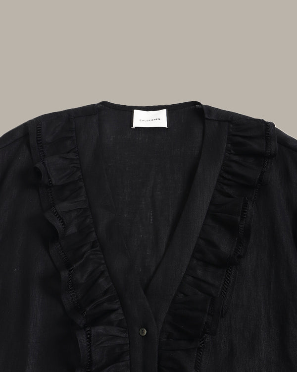 close up of a black ruffle blouse with ruffled details on a beige background