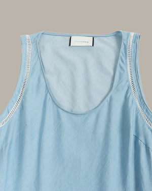 A close-up of a light blue sleeveless top with a wide scoop neckline and decorative white contrast stitching along the armholes, featuring a white brand label at the collar.