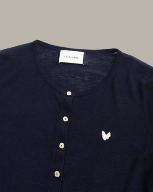 Close-up of a navy blue knit henley top by Chico's, featuring a white embroidered butterfly logo on the chest and a button-up front.