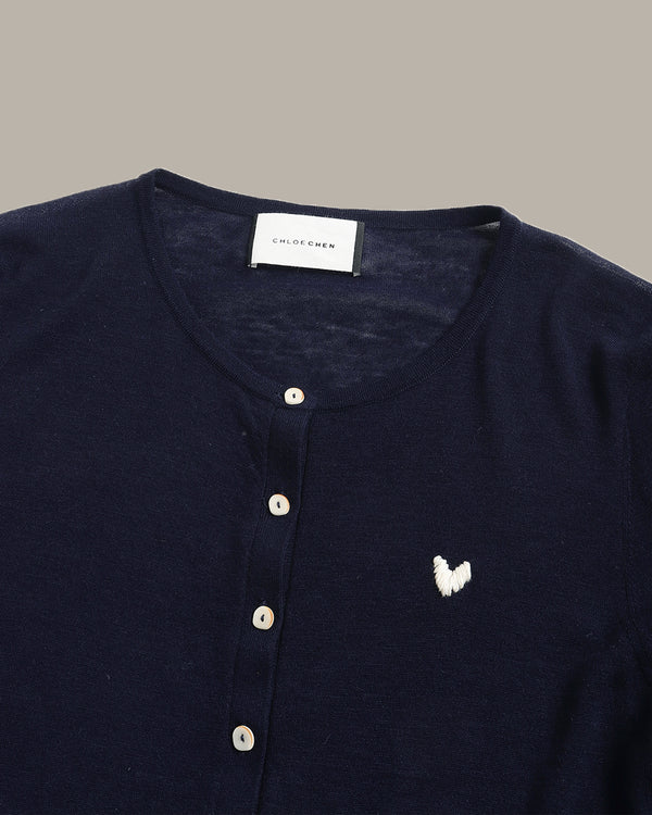 Close-up of a navy blue knit henley top by Chico's, featuring a white embroidered butterfly logo on the chest and a button-up front.