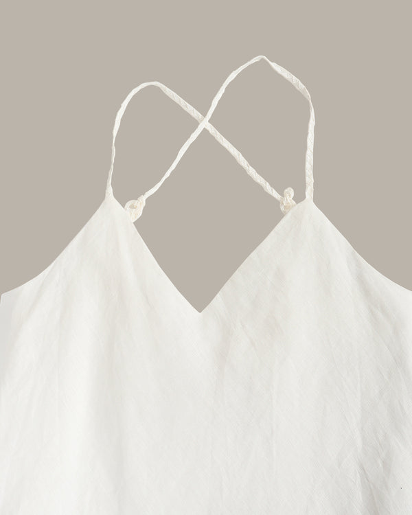 White cotton camisole top with thin adjustable spaghetti straps and knotted back details, shown against a solid taupe background.