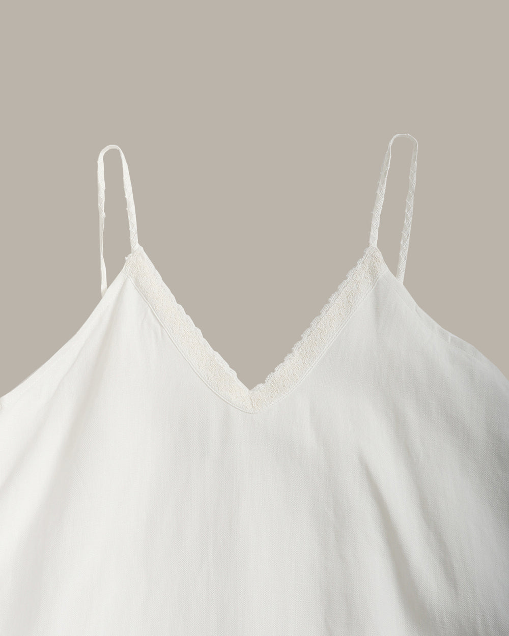 A white sleeveless slip dress with thin spaghetti straps and a V-neckline, shown against a solid taupe background.
