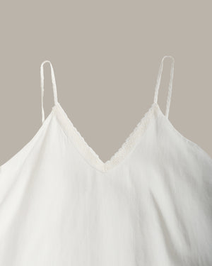 White camisole top with thin spaghetti straps and a delicate lace V-neckline, shown against a solid taupe background.