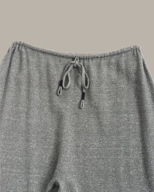 Close-up of a pair of heather gray knit pants showing the elastic waistband and drawstring closure against a solid taupe background.