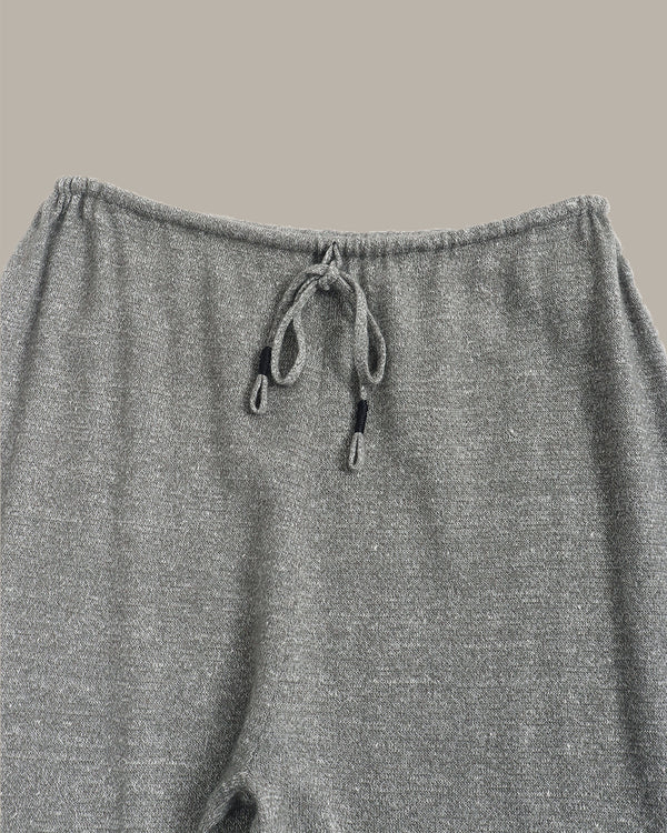 Close-up of a pair of heather gray knit pants showing the elastic waistband and drawstring closure against a solid taupe background.