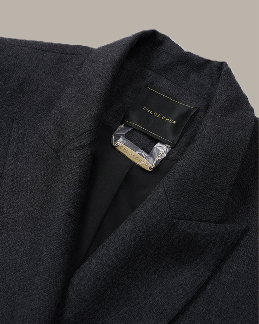 A dark charcoal gray double-breasted blazer with notched lapels and a subtle textured weave, displayed against a solid warm gray background.