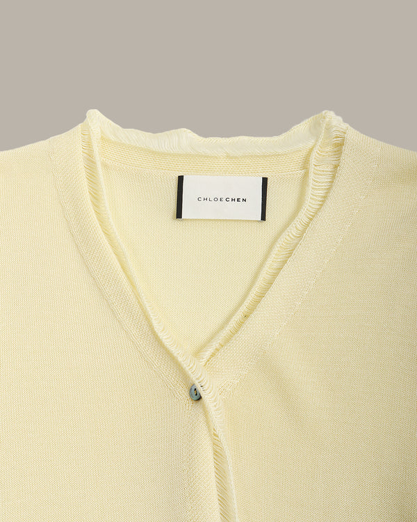 Light yellow cardigan with a brand label on a gray background
