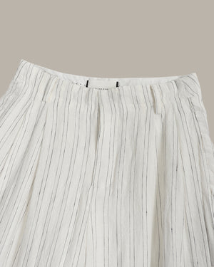 Close-up of pleated white pants with thin black stripes on a beige background