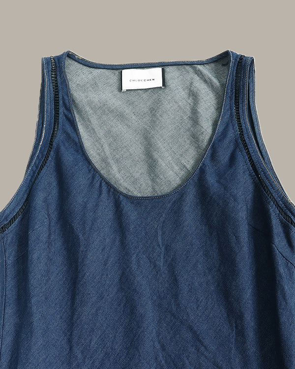 A close-up of a blue denim tank top showing the scoop neckline, dark contrast stitching, and a white brand label that reads 'SANCHEZ'.