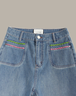 Close-up of a pair of light blue denim jeans showing the front waistband, button closure, and decorative embroidered details on the front pockets.