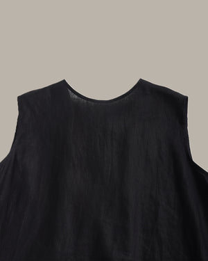 Close-up of a black sleeveless top or dress with a wide round neckline, shown against a solid taupe background.