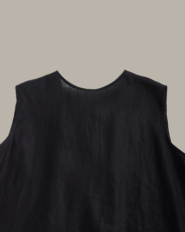 Close-up of a black sleeveless top or dress with a wide round neckline, shown against a solid taupe background.
