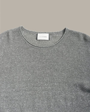 Close-up of a gray knit crewneck sweater with a white neck label reading 'SILK ROCKS', shown against a solid taupe background.
