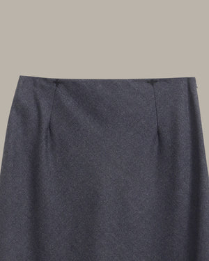 Close-up of a dark charcoal gray skirt fabric with a fine heathered texture, showing the waistband and side seam details against a solid taupe background.