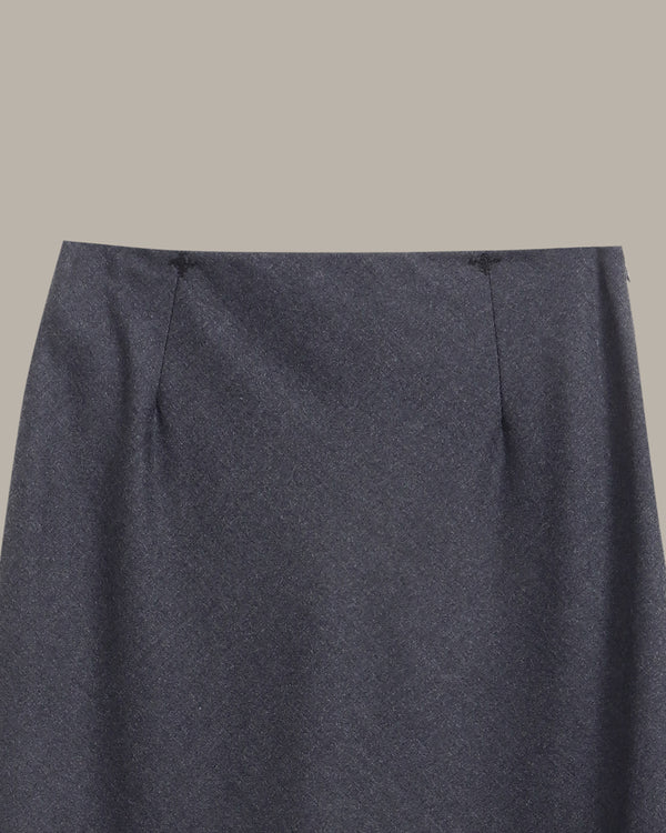 Close-up of a dark charcoal gray skirt fabric with a fine heathered texture, showing the waistband and side seam details against a solid taupe background.
