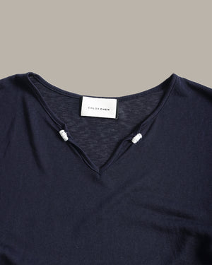 Close-up of a dark navy blue knit top with a split V-neckline and small white bead accents at the neckline. A white neck label reads 'CLOTHING'.
