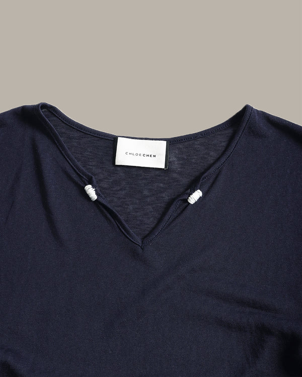 Close-up of a dark navy blue knit top with a split V-neckline and small white bead accents at the neckline. A white neck label reads 'CLOTHING'.