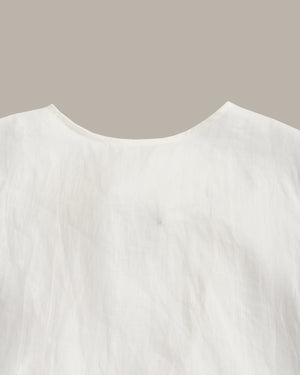 Close-up of a white textured fabric garment, showing a curved neckline against a solid taupe background.