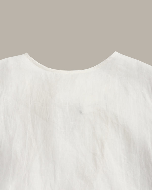 Close-up of a white textured fabric garment, showing a curved neckline against a solid taupe background.