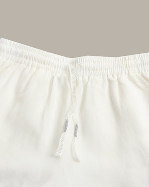 Close-up of white drawstring shorts showing the elastic waistband and drawstring details against a solid taupe background.