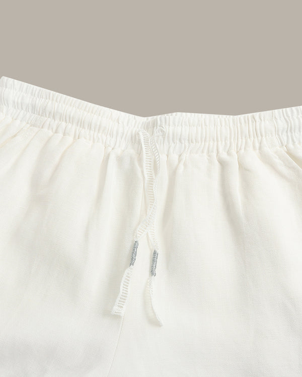 Close-up of white drawstring shorts showing the elastic waistband and drawstring details against a solid taupe background.