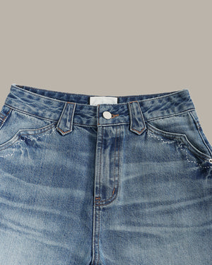 Close-up of the waistband and front pocket area of blue denim jeans on a plain warm gray background.