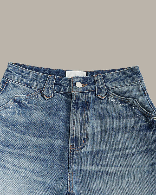 Close-up of the waistband and front pocket area of blue denim jeans on a plain warm gray background.