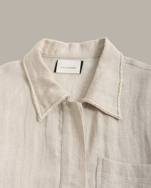 closeup of a linen jacket collar against a dark background with a plant.