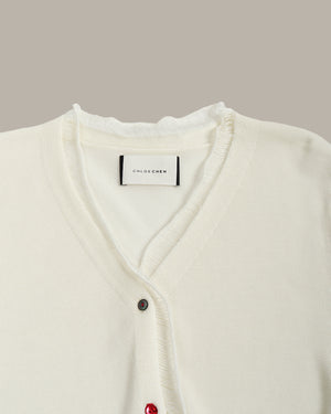 White cardigan with red buttons on a neutral background