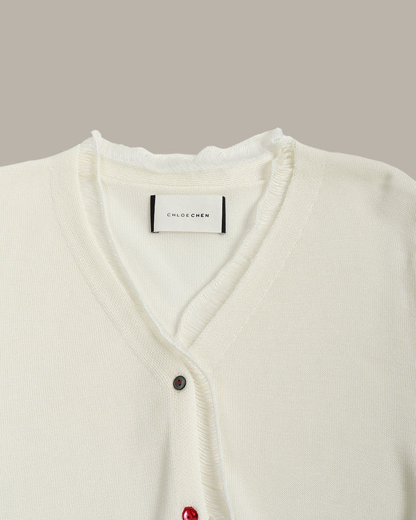 White cardigan with red buttons on a neutral background