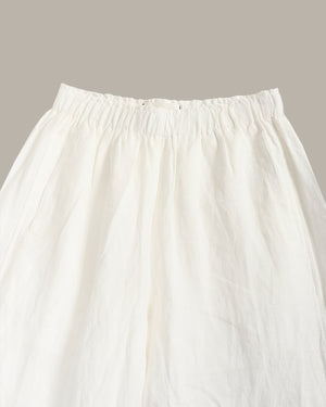 Close-up of a white or off-white skirt with an elasticized gathered waistband, shown against a plain warm gray background.