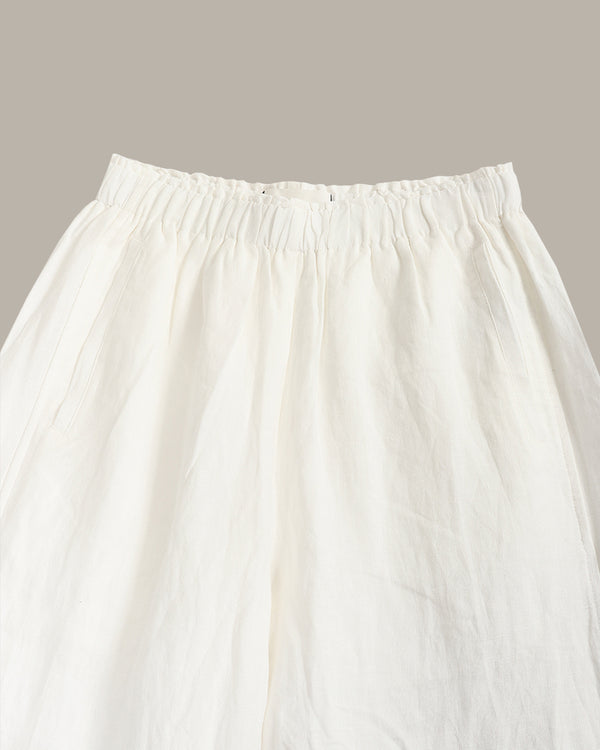 Close-up of a white or off-white skirt with an elasticized gathered waistband, shown against a plain warm gray background.