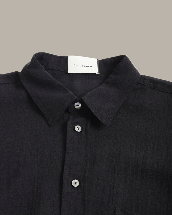 Black shirt with collar and buttons, featuring a visible brand label on a neutral background