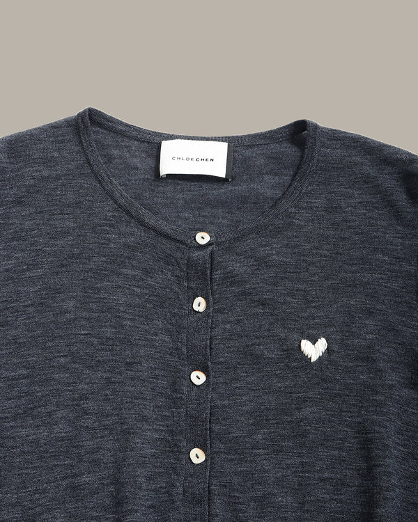 Close-up of a dark heather gray henley shirt with a white embroidered heart on the chest, featuring a button placket and a visible neck label that reads 'CLOUD QUEEN'.