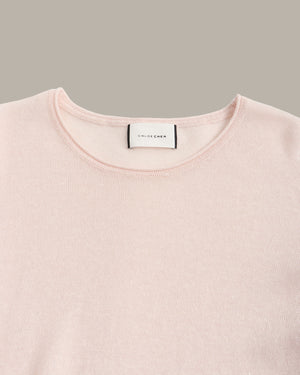 A close-up of a pale pink crewneck sweater by Chloé, showing the brand label at the collar against a solid taupe background.