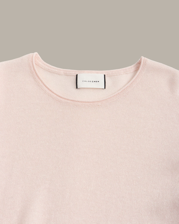 A close-up of a pale pink crewneck sweater by Chloé, showing the brand label at the collar against a solid taupe background.