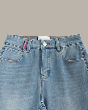 Close-up of the waistband and front pockets of light blue denim jeans against a solid taupe background.