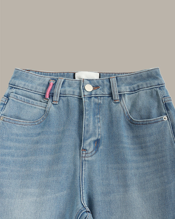Close-up of the waistband and front pockets of light blue denim jeans against a solid taupe background.
