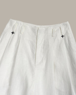 White pants with black floral embroidery on a neutral background