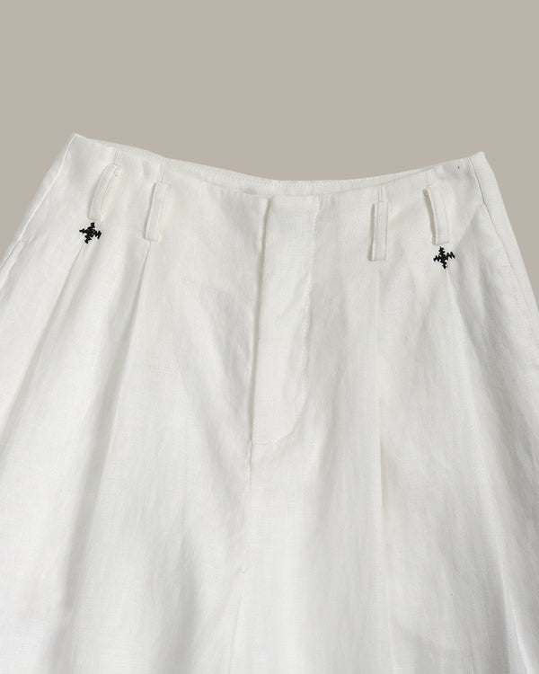 White pants with black floral embroidery on a neutral background